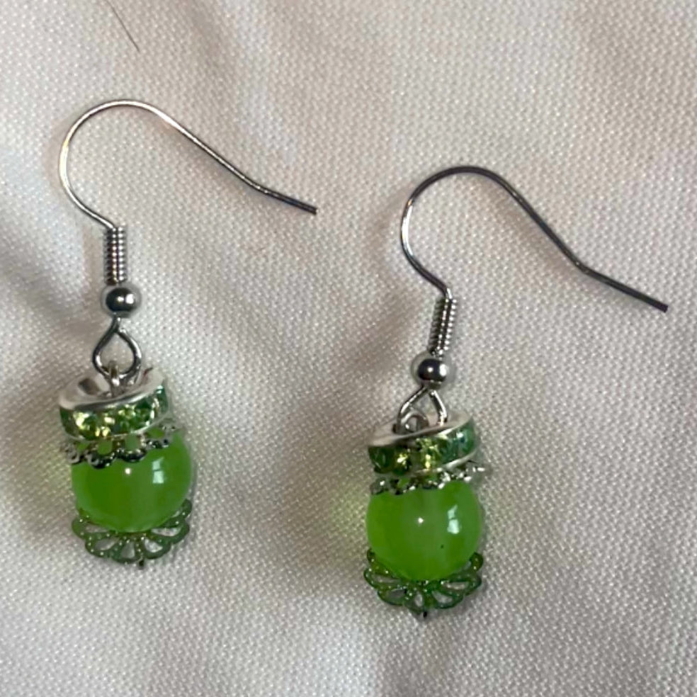Green beaded whimsical earrings with silver hooks on a white background