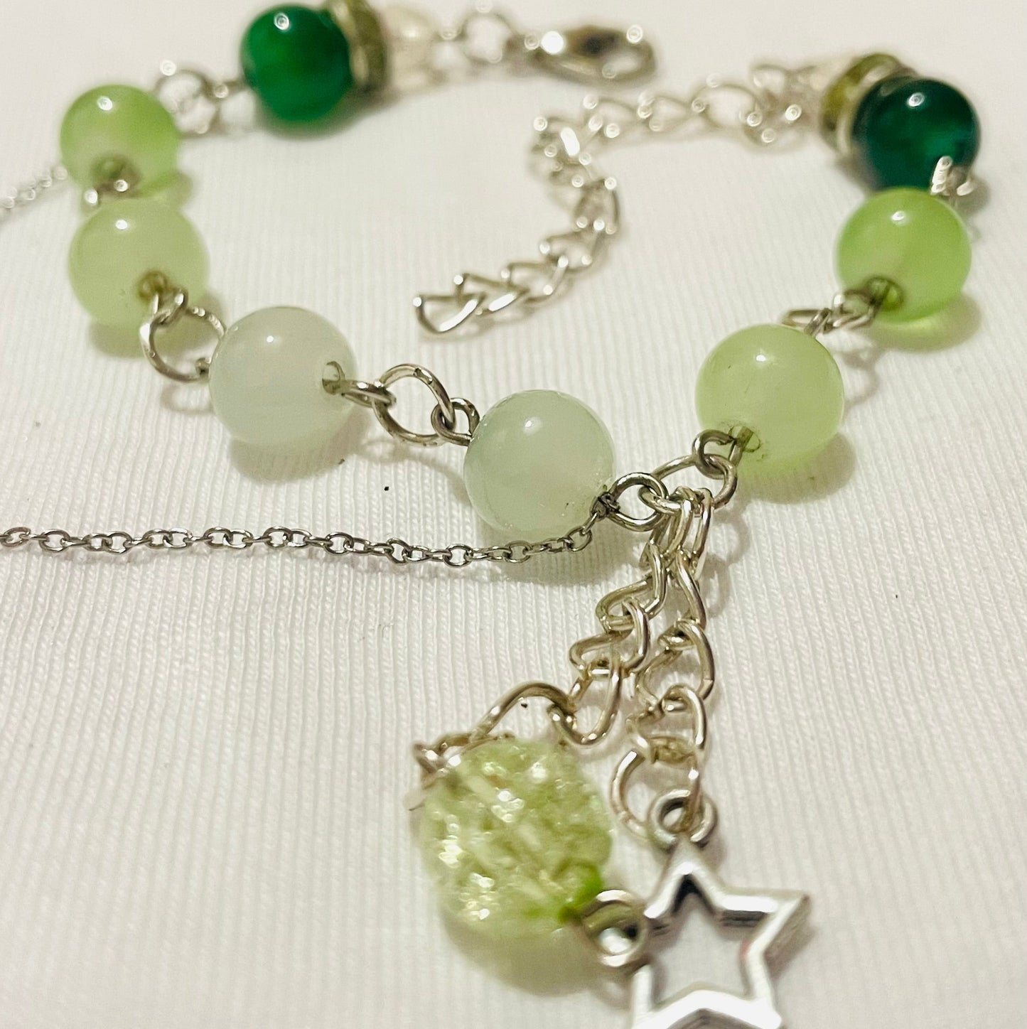 Green beaded cluster charm bracelet with star/ glass/ acrylic beads/ charms with silver touches on a beige background