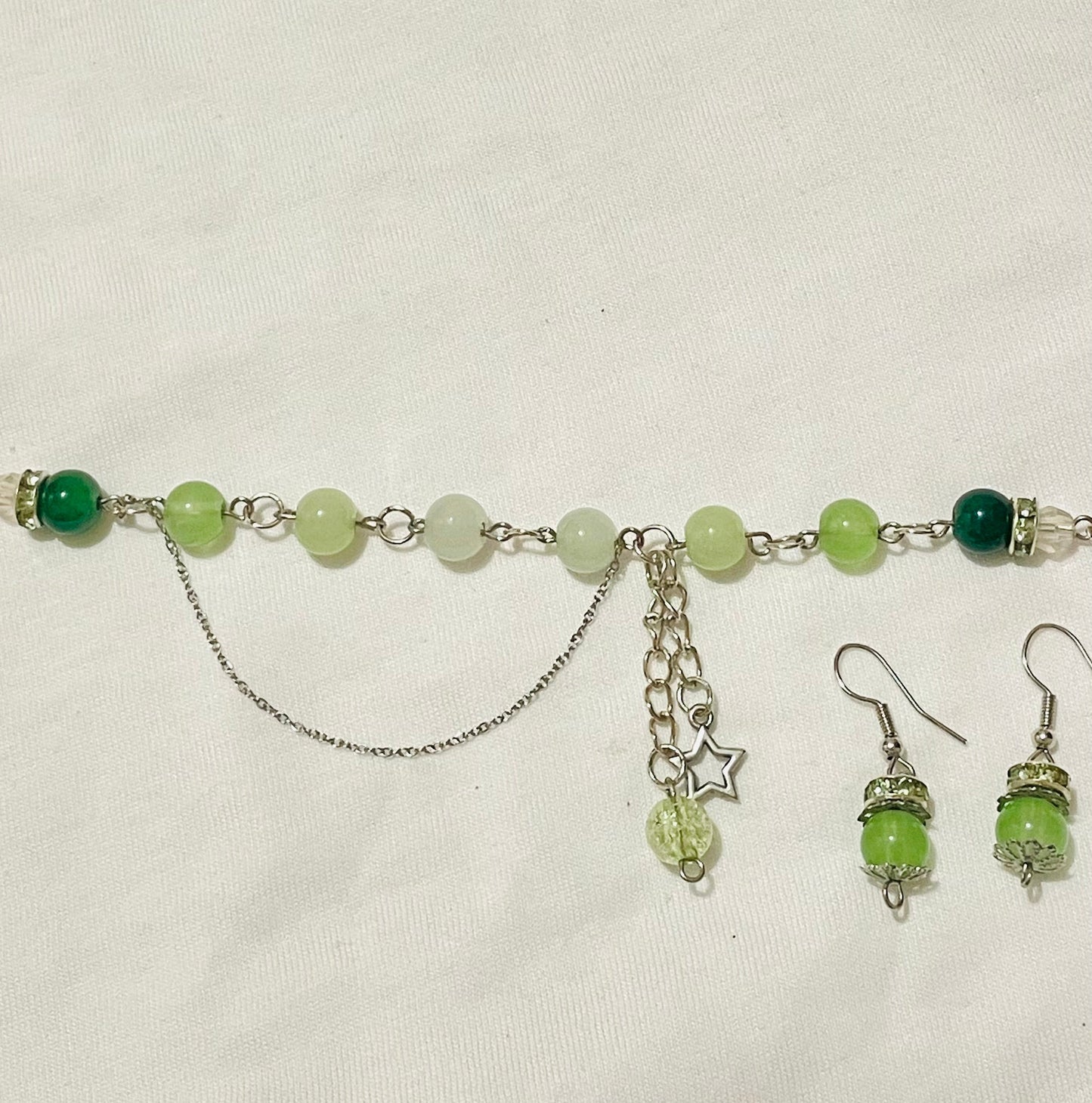 Green beaded cluster charm bracelet with star/ glass/ acrylic beads/  charms and matching green earrings with silver touches on a beige background