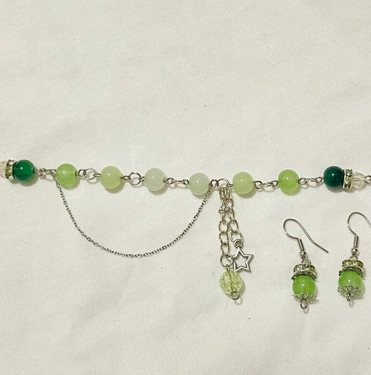 Green beaded cluster charm bracelet with star/ glass/ acrylic beads/  charms and matching green earrings with silver touches on a beige background