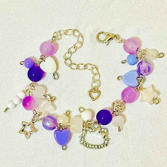 Purple beaded cluster charm bracelet with star/ glass/ acrylic beads/ hello kitty charm/  charms on a beige background