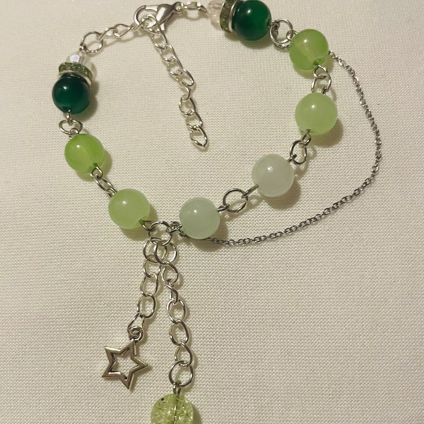 Green beaded gradient bracelet with a star charm and sparkly bead and a short minimal chain on a light background