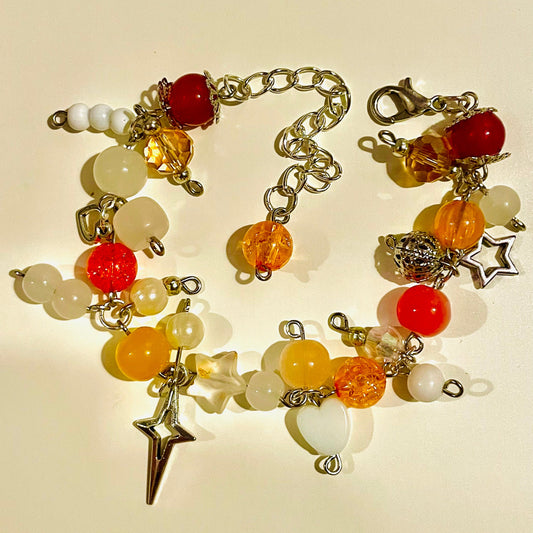 Fall themed orange/red beaded cluster bracelet with star/ glass/ acrylic beads/ charms on a beige background